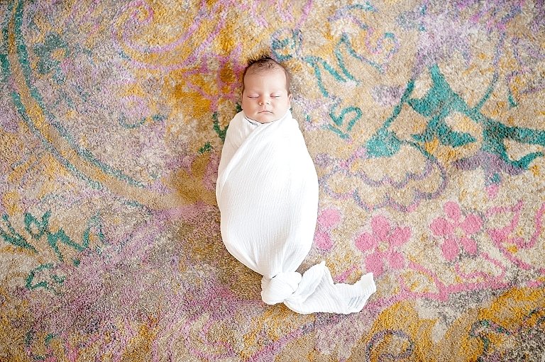 Baby lays swaddled on a brightly colored rug