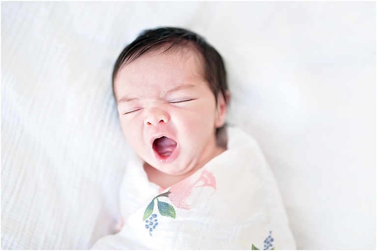 newborn baby girl yawns while swaddled