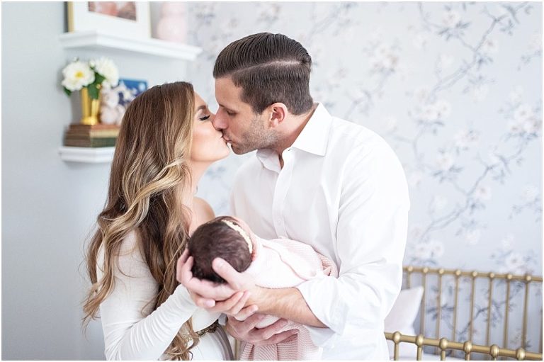 mom and dad kiss while holding newborn